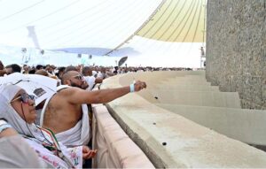 Hajj pilgrims throwing pebbles at three pillars that represent Satan at Jamarat while performing Hajj ritual