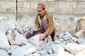 A mason making building blocks from stone on the road side of Chinar Bagh River View Road.
