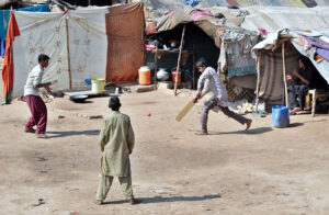 Nomadic boys playing cricket outside their makeshift houses at the roadside in the City.
