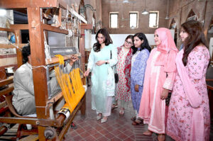 Women watching cloth being woven on a loom in exhibition at National Heritage Museum.