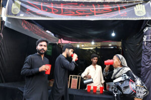 Volunteer serving drinks to the mourners at Sabeel during Muharram-ul-Harram outside Qadamgah.
