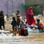 A Gypsy family washes clothes while children enjoy bathing in a water canal to escape the hot weather in the city