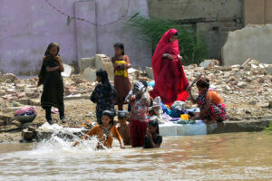 A Gypsy family washes clothes while children enjoy bathing in a water canal to escape the hot weather in the city