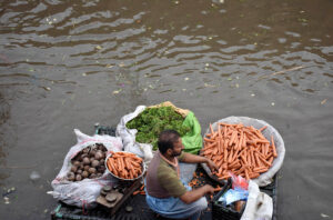 A labourer sitting on the potatoes and Onion sacks after unloading from the delivery truck as the rain water accumulated at fruit and vegetable market after heavy rain that experienced in the Provincial Capital.