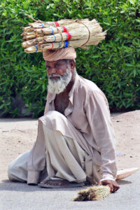 An elderly vendor displaying the brooms to attract the customers at Latifabad.