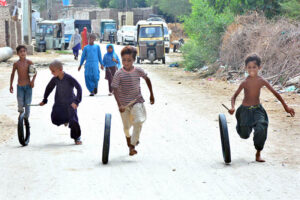 Children turning waste tires into playthings, running barefoot along the roads of Latifabad.