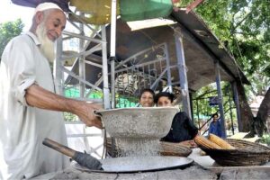 An elderly vendor roasting corn cob for customers at his roadside setup in Federal Capital