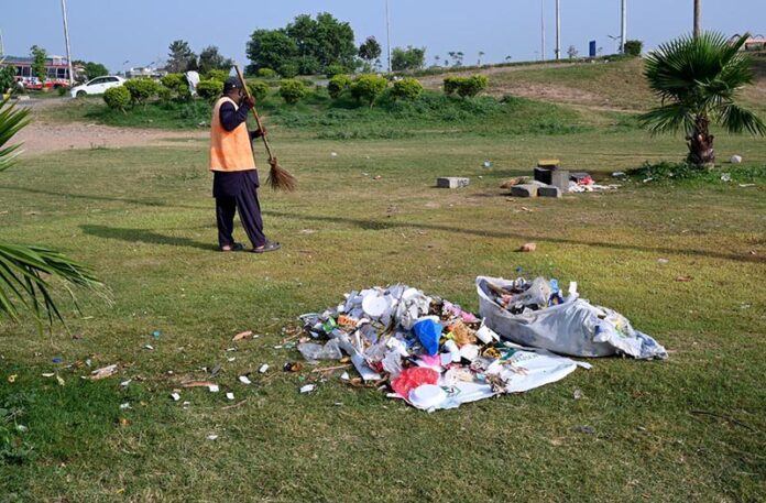 A CDA sanitary worker cleans garbage at the green patch of Faizabad Interchange after Tekreek-e-Labbaik Pakistan called off its week-long protest sit-in