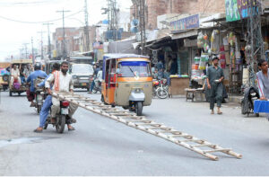 A person holding a ladder while sitting on the rear seat of a motorcycle on the Vehari Road.