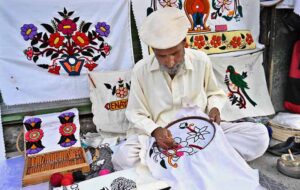 A worker busy in embroidery work on pillow and bed sheet at his setup.