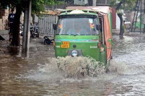 Motorcyclists and auto rickshaw passing through rain water accumulated on road after rain in the Provincial Capital