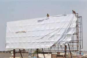 Laborers fixing a huge advertisement banner on a billboard without safety measures at Chungi No 09