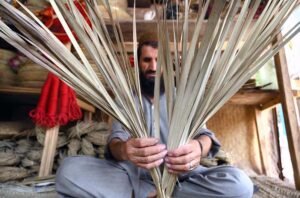 A worker is busy making handicrafts with date palm leaves at his shop.