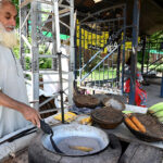 An elder vendor roasting corn cob for selling at his roadside setup