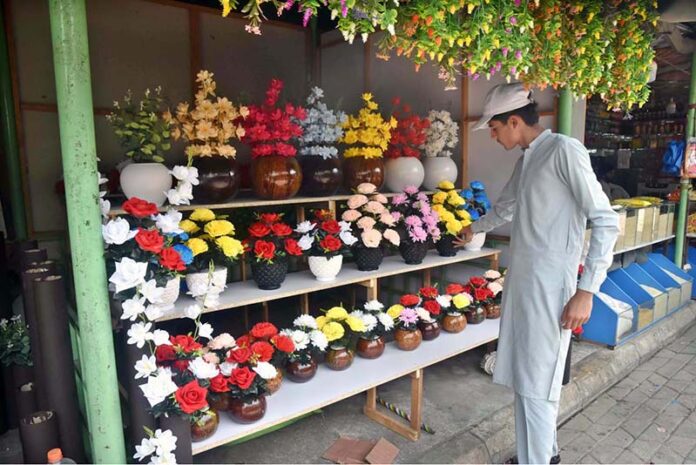A vendor arranging and displaying artificial flower to attract the customers outside weekly Sunday Bazaar setup in H-9 Sector in Federal Capital