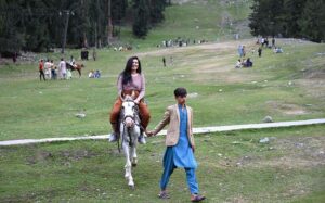 A woman tourist enjoying horse ride at Nalter Valley, a popular tourist destination, as a large number of other people have also arrived to visit the area