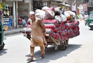  Laborer pulling his hand cart heavily laden with pillows to deliver in the  market at Dabgari area.