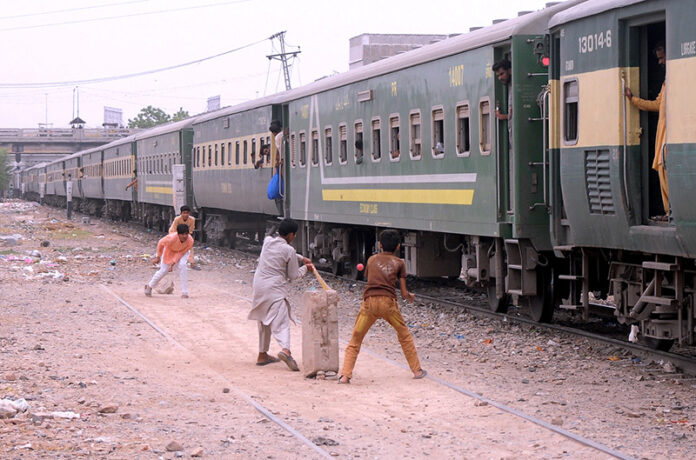 Cricket enthusiasts enjoy the game near the rail track with a passing train