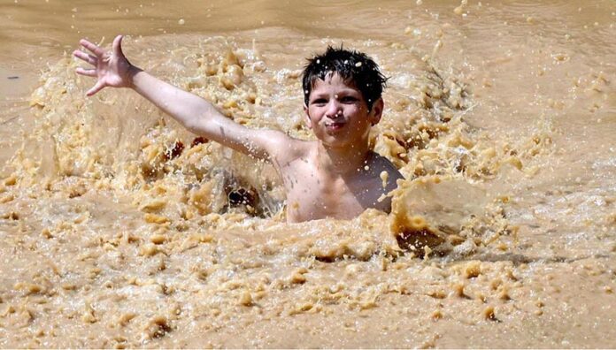 A youngster jumping and bathing in stagnant rain water accumulated in pond to get some relief from hot weather in the Federal Capital