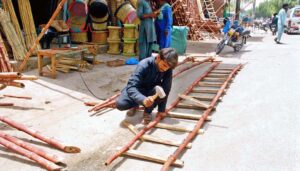 A carpenter is preparing bamboo ladder outside his shop in a local market.