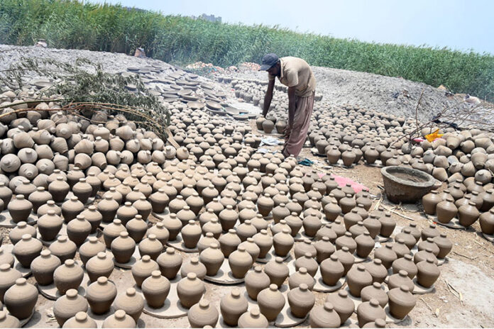 A worker arranging clay-made stuff for draying purpose at his work place at Kumharpara