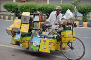 An elderly person on the way along with his bicycle loaded with empty ghee tin after collecting from different points to earn livelihood by selling them in the junkyard.