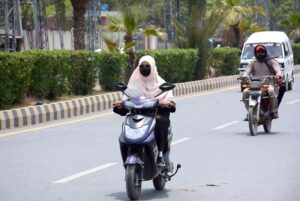 A woman is riding a scooter to her destination under the scorching sun in the city.
