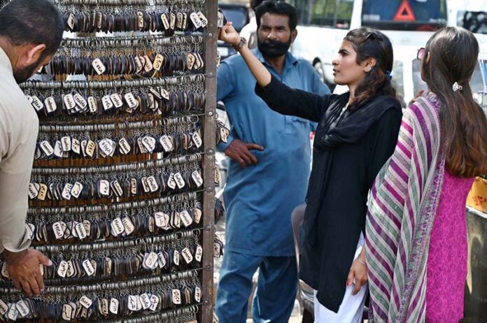A girl selecting and purchasing keychain with her name from vendor at famous picnic spot Daman-e-Koh
