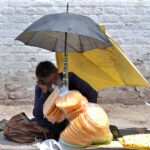 An elderly person waiting for customers to sell saltish item (papar) while sitting under shadow of an umbrella at LMQ Road