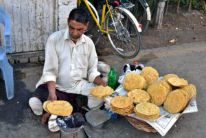 A vendor skillfully roasts papadam over an open flame on the roadside, enticing passersby with its aromatic allure at Baghe Jinnah in the Provincial Capital.