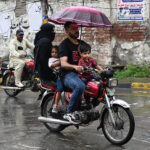 A man shields his family from the rain with an umbrella while riding a motorcycle in the Provincial Capital