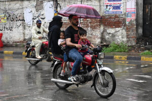 A man shields his family from the rain with an umbrella while riding a motorcycle in the Provincial Capital