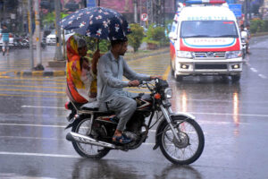 A man shields his family from the rain with an umbrella while riding a motorcycle in the Provincial Capital