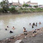 People bathing in running tub well to get relief from scorching hot weather in the city