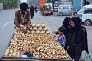 Children pick out Golak (money-boxes) and toy pots from a vendor's cart adorned with golden pots, set up on the streets near Bibi Pak Daman.