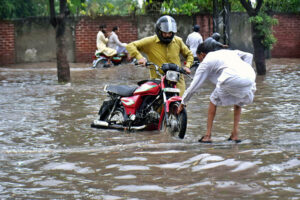 Motorcyclists stuck in water are struggling to move their bikes to the other side from the submerged road during the heavy rain in the provincial capital.