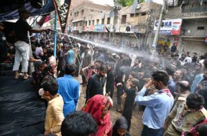 Volunteer showering water on mourners attending Youm-e-Ashura procession on 10th of Holy Month of Muharramul Harram at Station Road to keep them cool during hot and humid weather in the city.