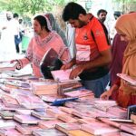Women selecting and purchasing old books from a roadside stall at Mall Road in the Provincial Capital