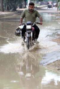 Motorcyclist passing through accumulated rain water on a road after monsoon rain at the metropolis.