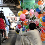 A street vendor displaying balloons to attract customers while sitting on the roadside at Liaquat Bagh