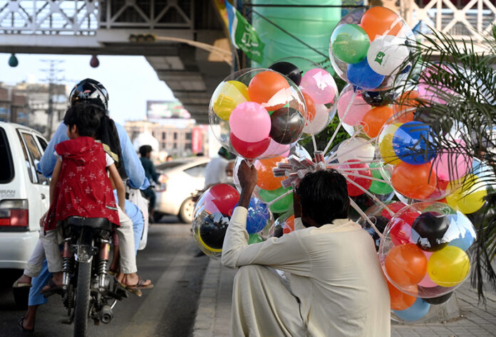 A street vendor displaying balloons to attract customers while sitting on the roadside at Liaquat Bagh