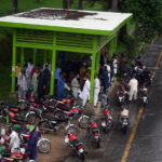 Motorcyclists take shelter at a bus terminal at Zero Point during heavy rain in the Federal Capital