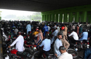 Motorcyclists take shelter at a bus terminal at Zero Point during heavy rain in the Federal Capital
