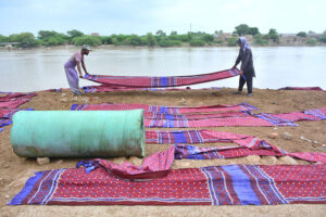 Labourers busy in spreading Sindhi ajrak for drying near water canal.