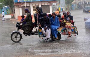 Gypsy women with children traveling on the tri-cycle rickshaw during rain in the city.