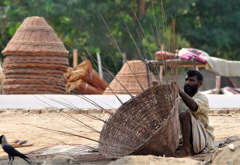 Artisan preparing a basket with dry tree branches to sell for livelihood at roadside