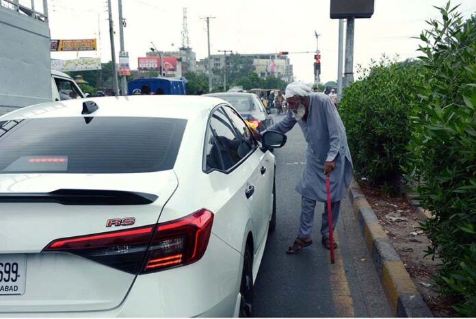 An elderly beggar begs from auto drivers near traffic junction on Jaranwala Road