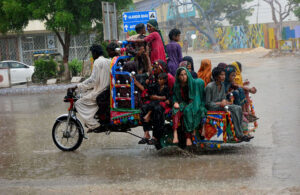 Gypsy women with children traveling on the tri-cycle rickshaw during rain in the city.
