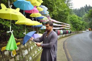 A street vendor displays colorful umbrellas aiming to attract customers for selling at his roadside setup on Dunga Gali Road.