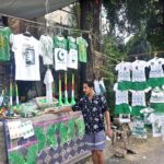 A vendor arranging and displaying national flags, shirts and dresses for children in connection with upcoming Independence Day celebrations at his roadside setup in Federal Capital